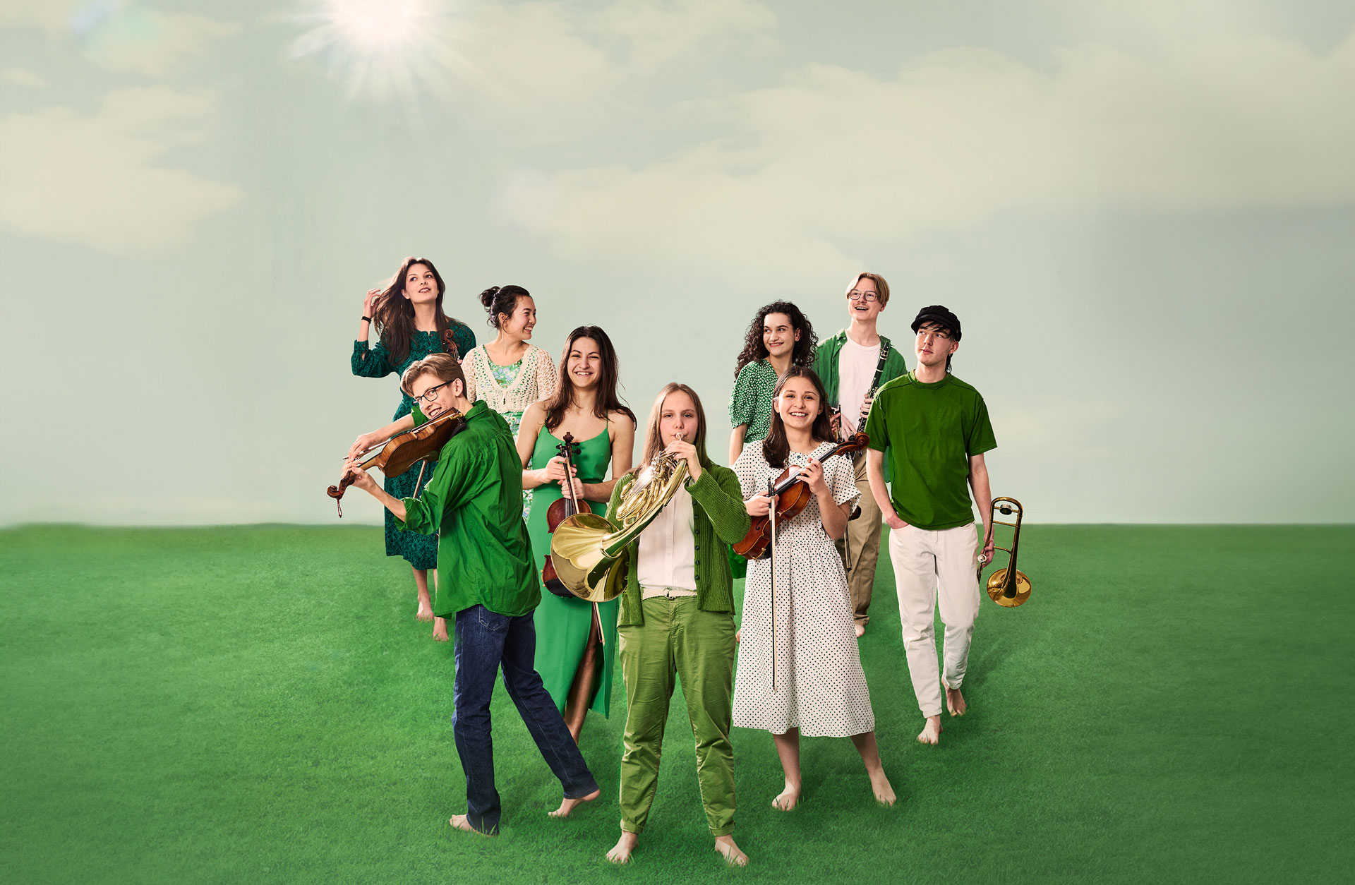 9 glada ungdomar med instrument står på en gräsmatta. De är alla klädda i olika gröna kläder.