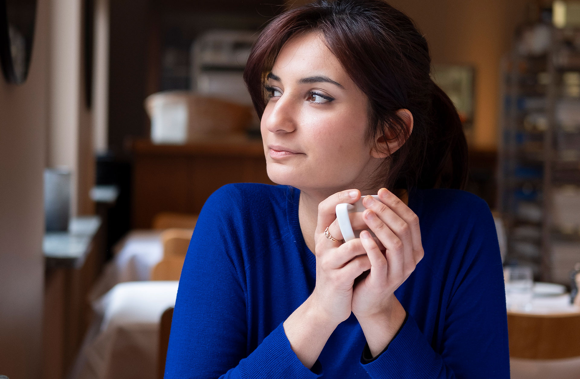 Ava Bahari sitter med en kaffekopp i händerna. Hon sitter i Konserthusets restaurang och hon tittar ut genom fönstret.