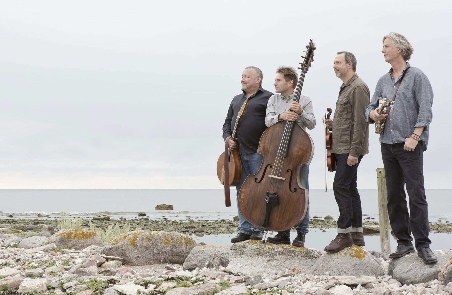 De fyra musikerna i Quilty står på en strand vända i profil. De håller i sina instrument.