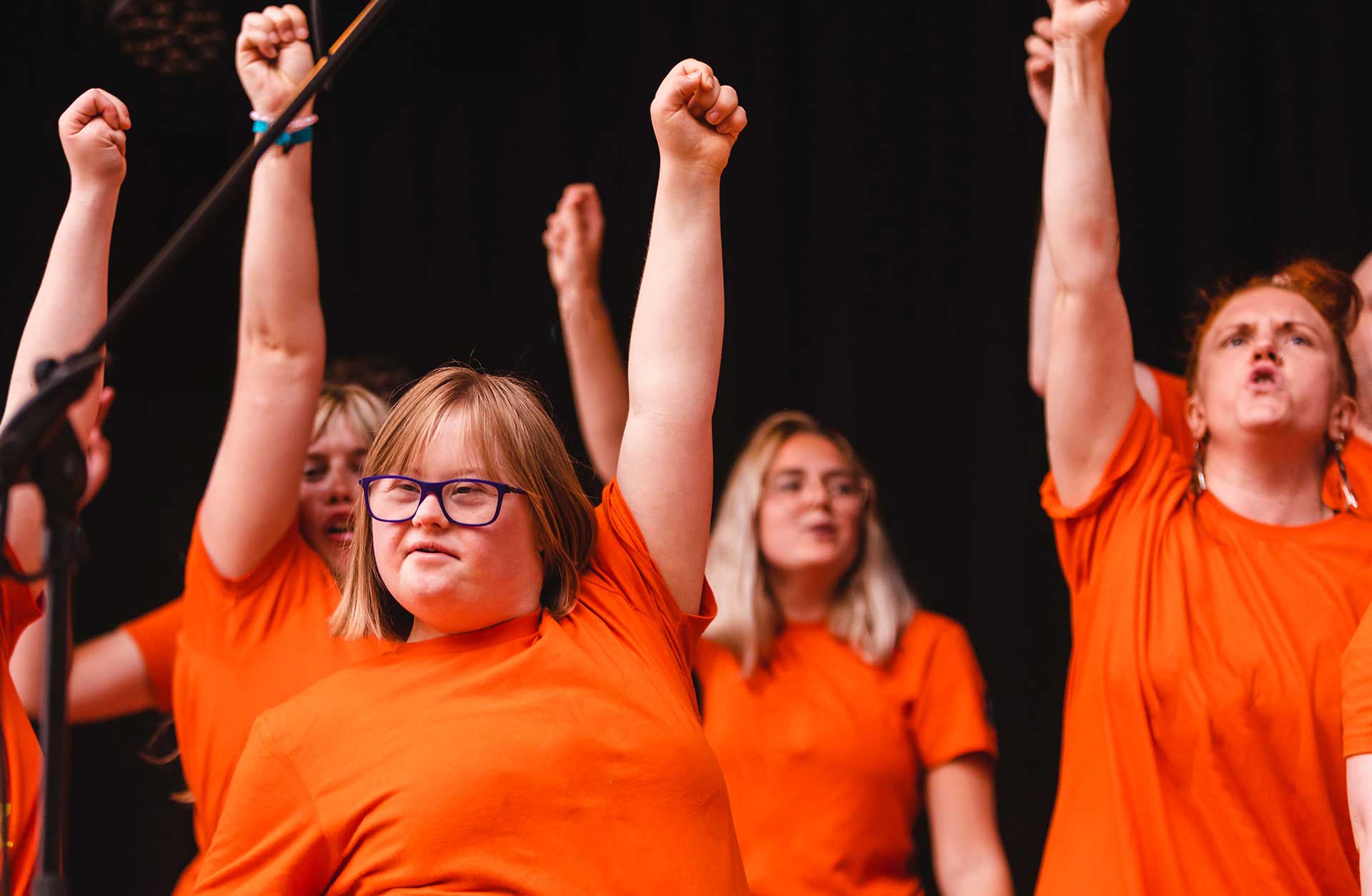 En kör med orange tröjor med armarna uppsträckta.