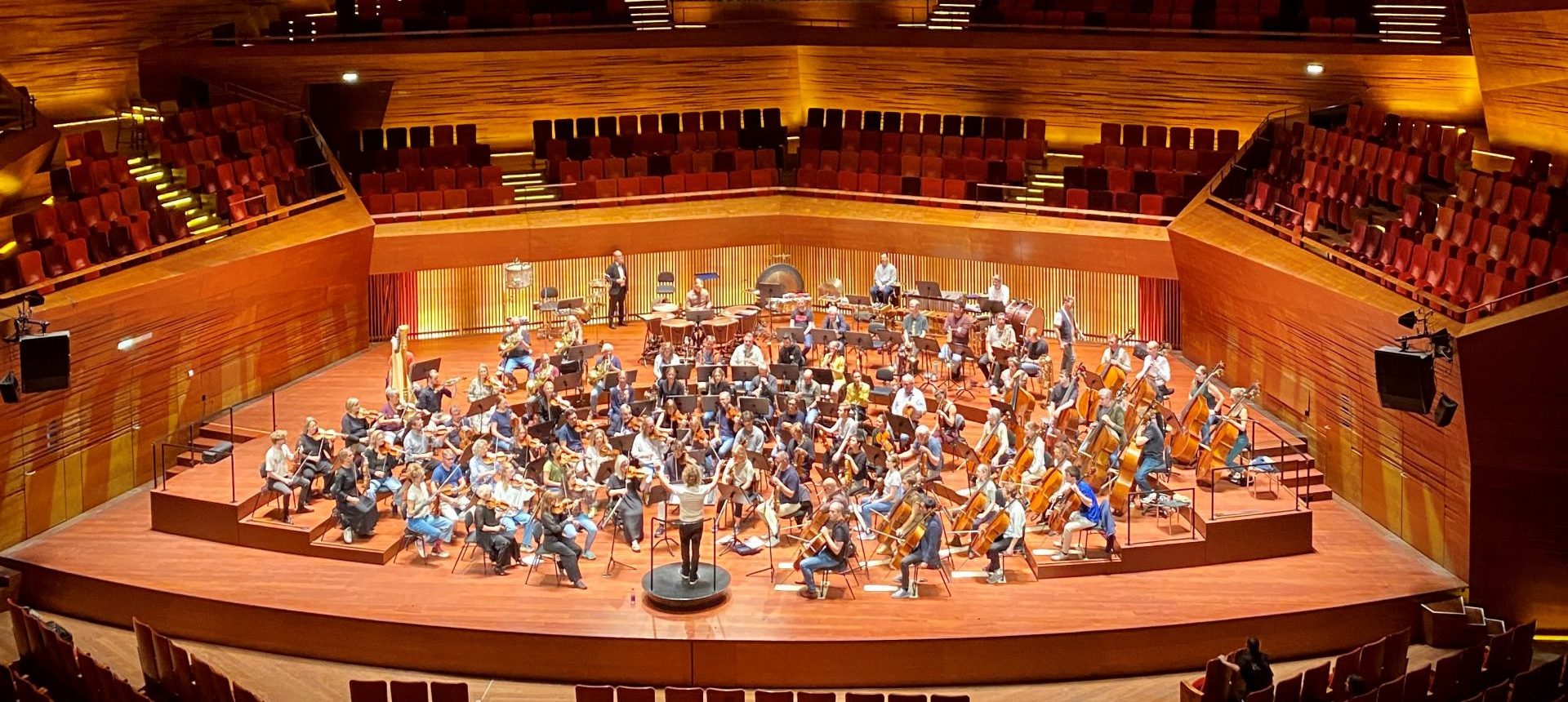 Bild ovanifrån i Danmarks Radio Konserthus med orkestern sittandes ner på scenen med sina instrument.